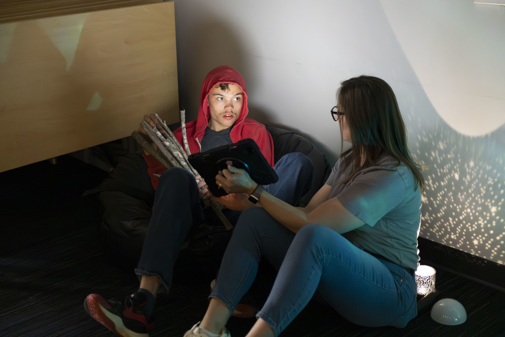 Young man holding sticks attending to a communication partner holding an ipad. 