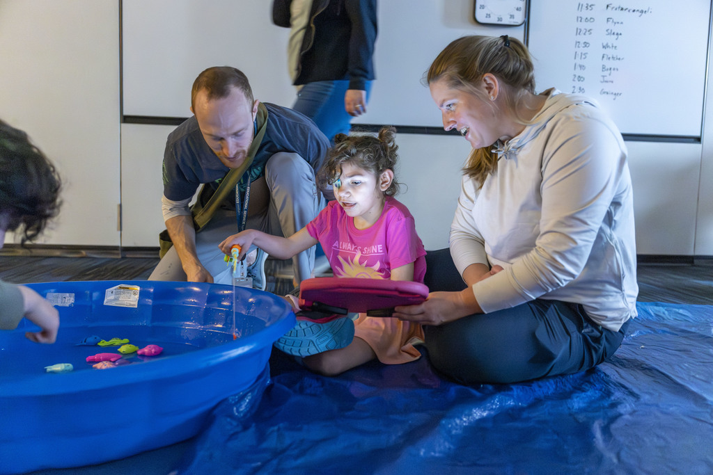 Two adults with a young girl who is fishing in a swimming pool. 