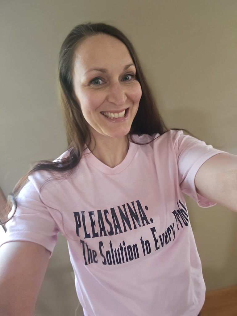 A selfie of the same smiling woman wearing a light pink t-shirt. The shirt has bold black text that reads, "PLEASANNA: The Solution to Every Problem."