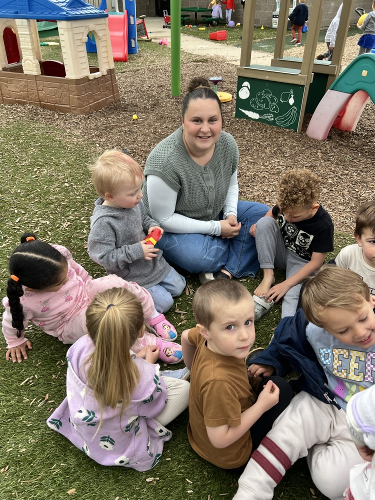 Young woman sitting on ground surrounded by small children 