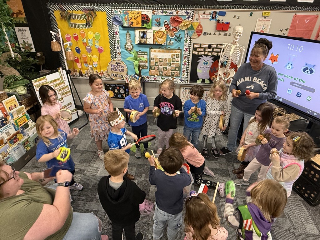A preschool teacher leads a circle of children in a classroom as they explore and play different musical instruments together.