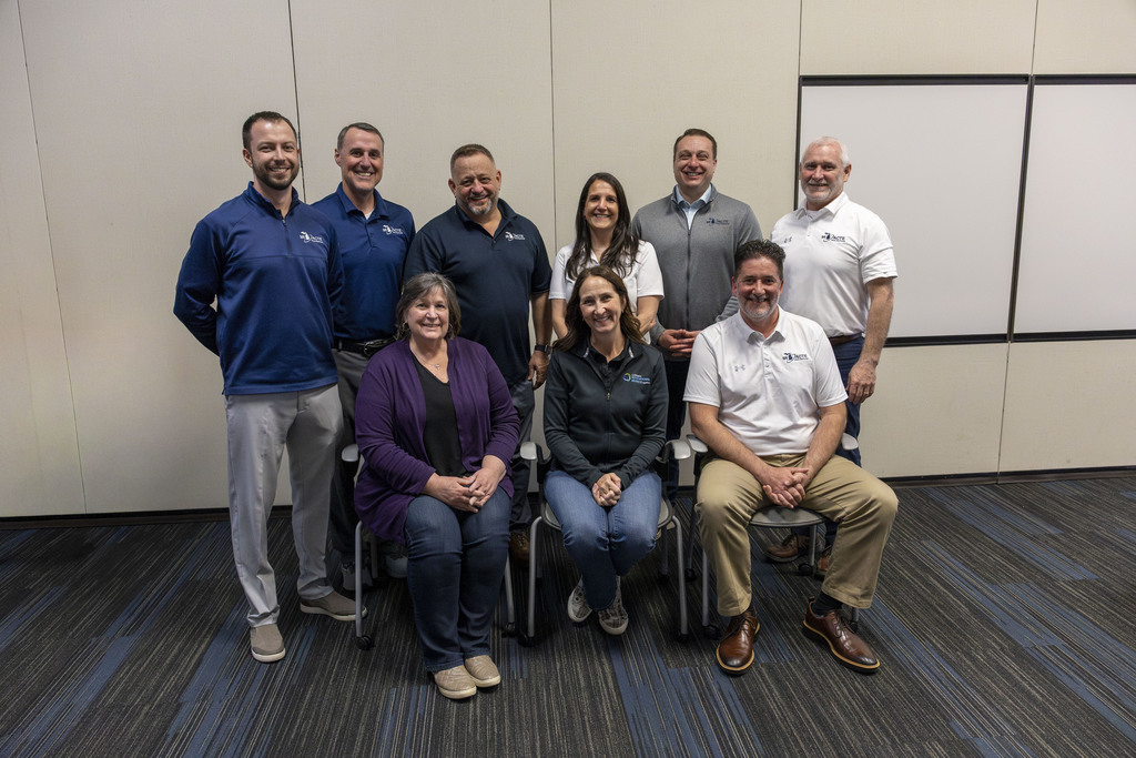Nine adults pose for a group photo, 6 standing and 3 sitting.