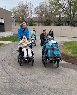 Two female staff members push students in wheelchairs around a track