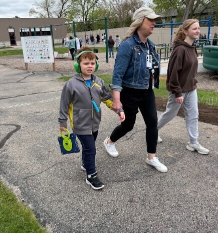 A young boy holds a staff member's hand while walking around an outdoor track.