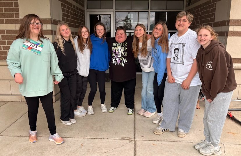 A group of  students in a semi-circle smiling at the camera with their arms around each other.