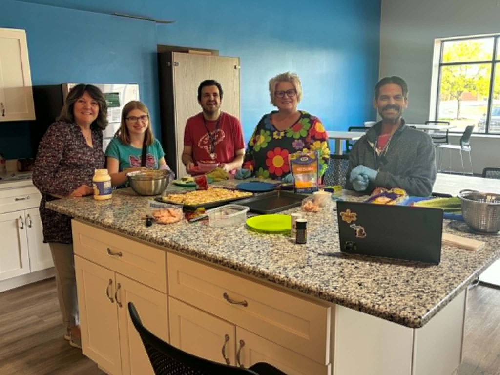 Staff and students smiling together while preparing food for the upcoming PREP graduation celebration.