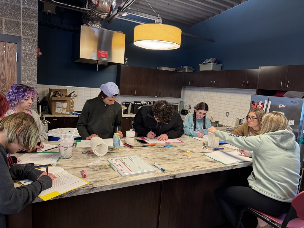 Group of students sit around a a large counter writing in notebooks.