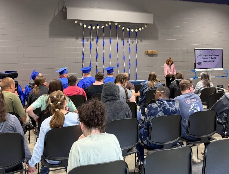 An adult female stands at a podium speaking to a group of students during a graduation ceremony.