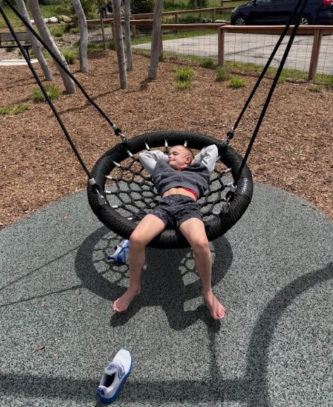 a young boy lays in a relaxed manner on a round netted swing with his hands behind his head