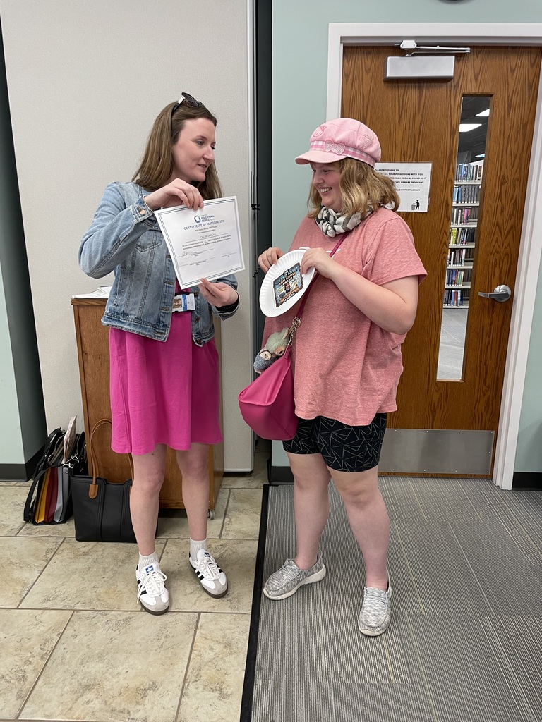 A female teacher handing an award to a young female adult learner.