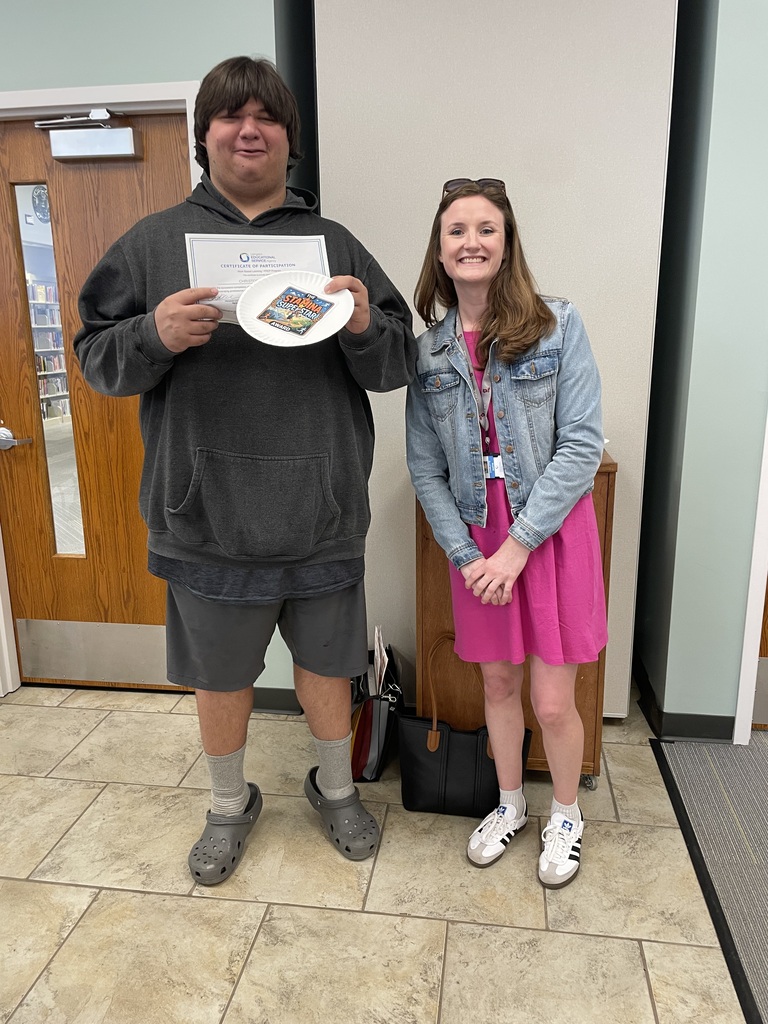 A young adult male holding an award, standing next to a female adult.