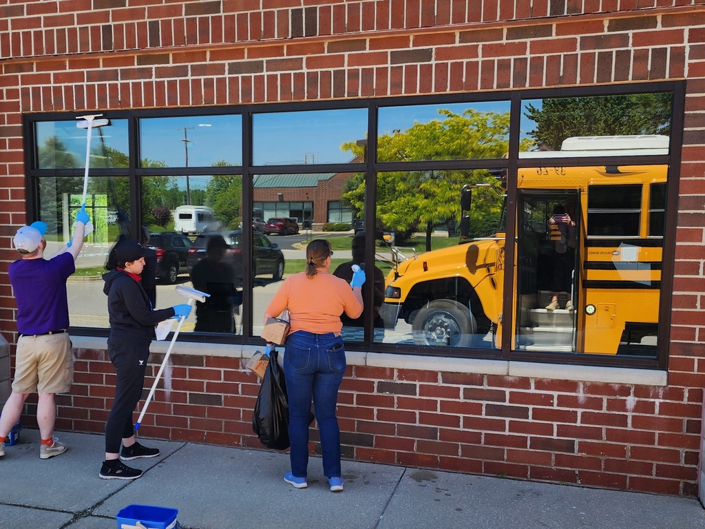 One male and one female, young adult learners and a teacher cleaning the outside windows of their business like building.