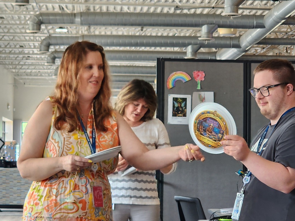 Two female teachers giving an award to a young male adult learner,