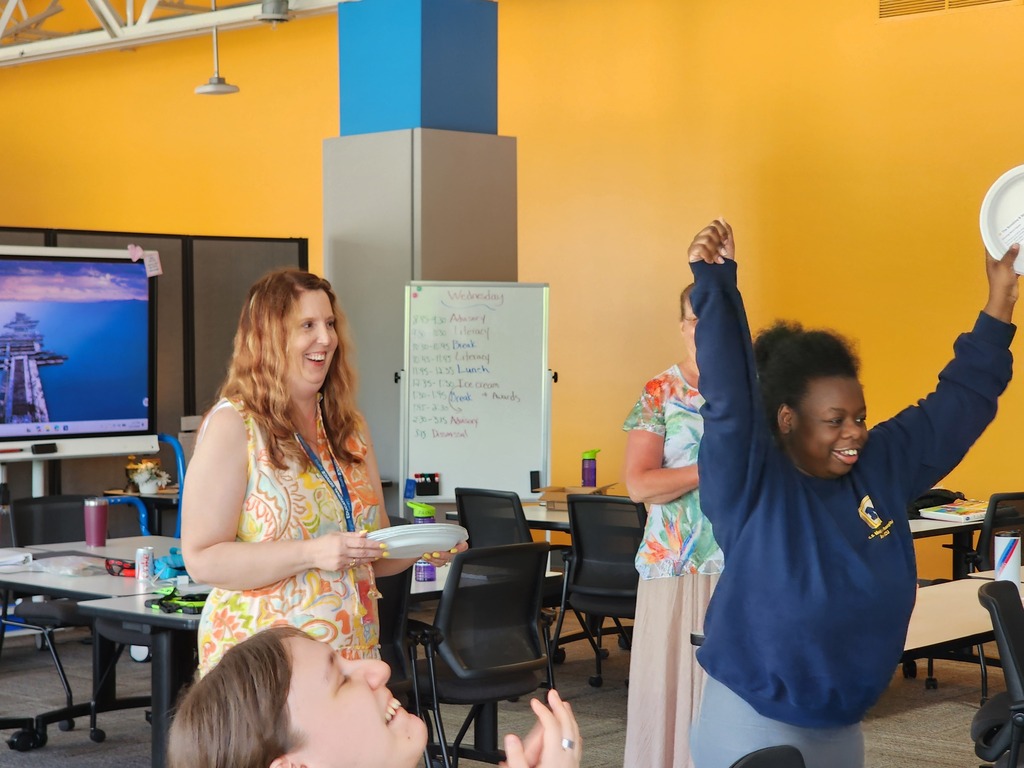 A young female learner shakes her arms up in joy as a female teacher looks on.