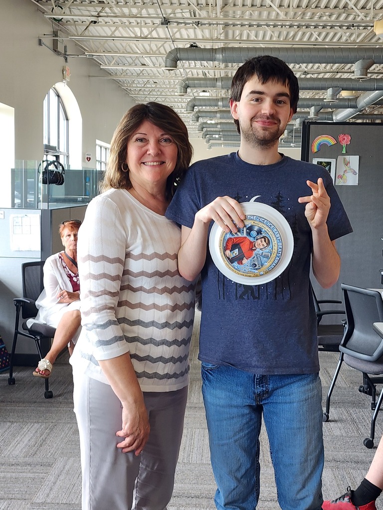 A young adult male learner happy showing off his award while standing next to a female teacher.