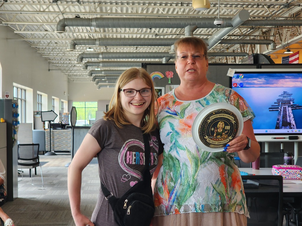 A female young adult learner and a teacher stand next to each other as an award is presented to the learner.