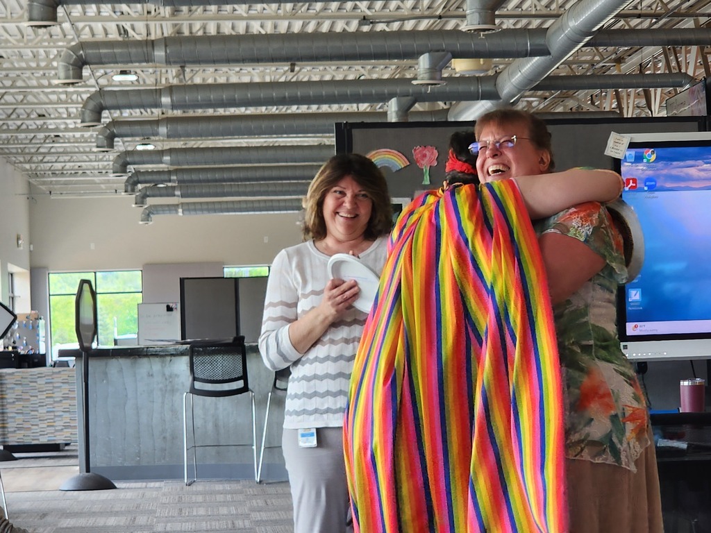 A  young adult female learner has a celebratory hug with a female teacher as another female teacher looks on.