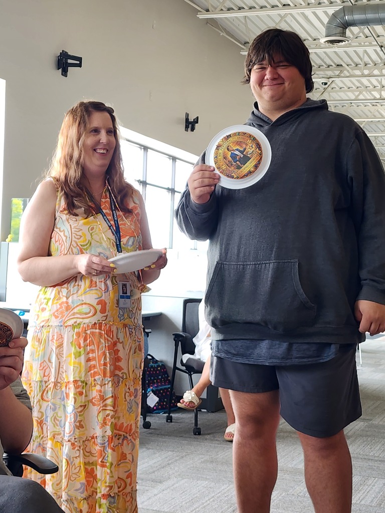 A female teacher standing next a tall, young male adult learner holding his award.