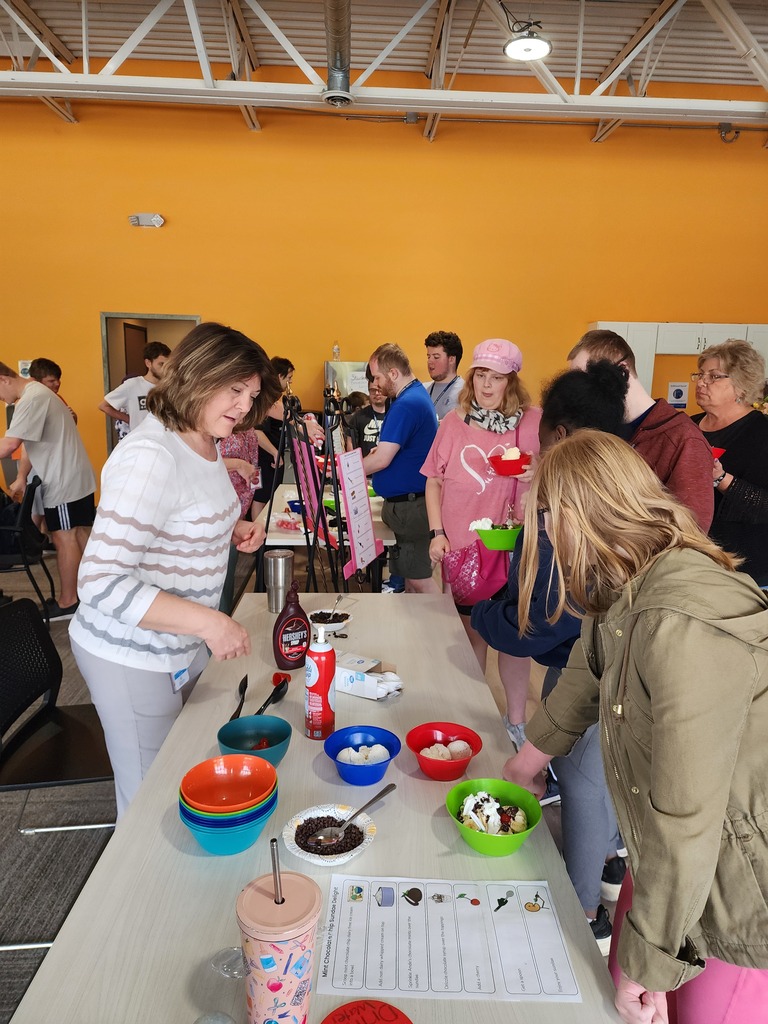 Many male and female staff and adult learners building ice cream sundaes around a table.