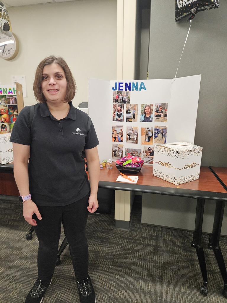 Jenna stands smiling next to her graduation display board, which features a collection of photos showcasing her work at Trinity Health.