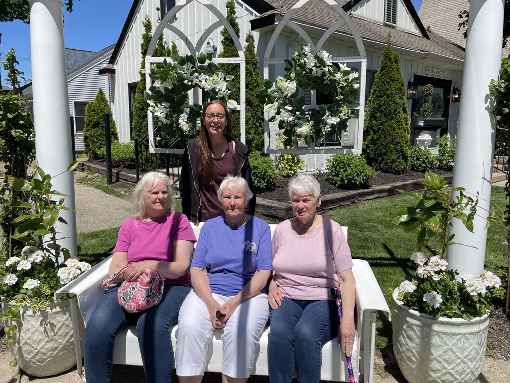 Three ladies sitting on a bench and one lady standing behind them.