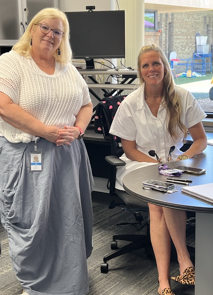Two women, one standing-one sitting at a desk 