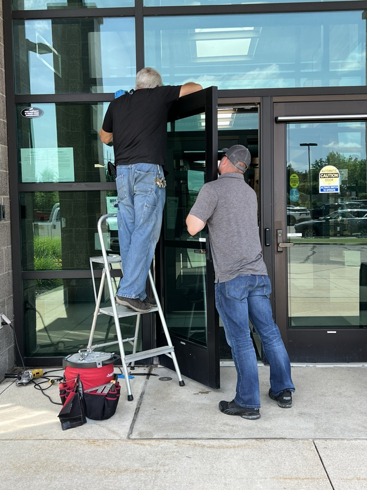Two men fixing a door, one on a stepladder the other holding the door 