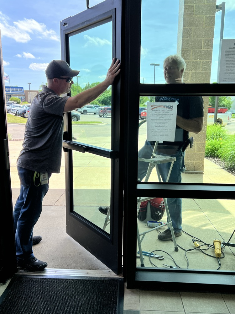 Two men fixing a door, one on a stepladder the other holding the door.