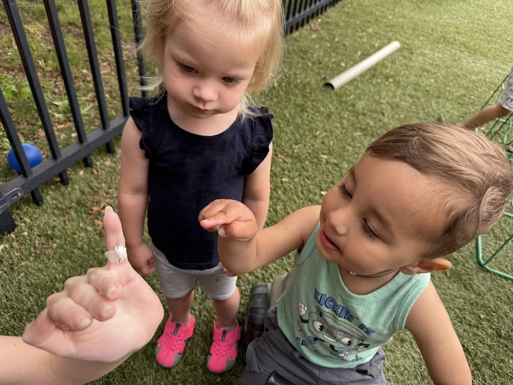 Two children gather around an adult's hand to closely examine a small insect they discovered while playing outside.