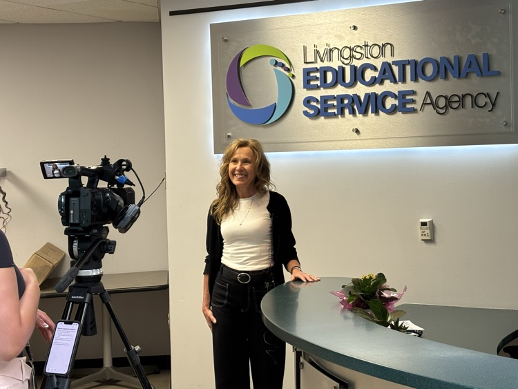 Woman stands in front of LESA sign while being interviewed by CBS News Lansing.