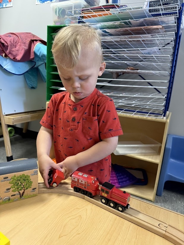 Young child plays with toy trains on a wooden track while exploring how the pieces connect.