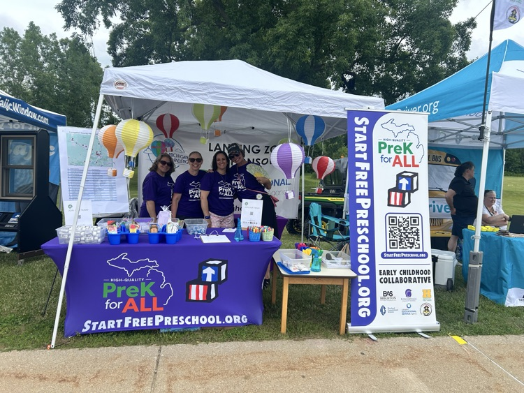 Group of women in matching purple shirts inside a tent with a table branded for StartFreePreschool.org