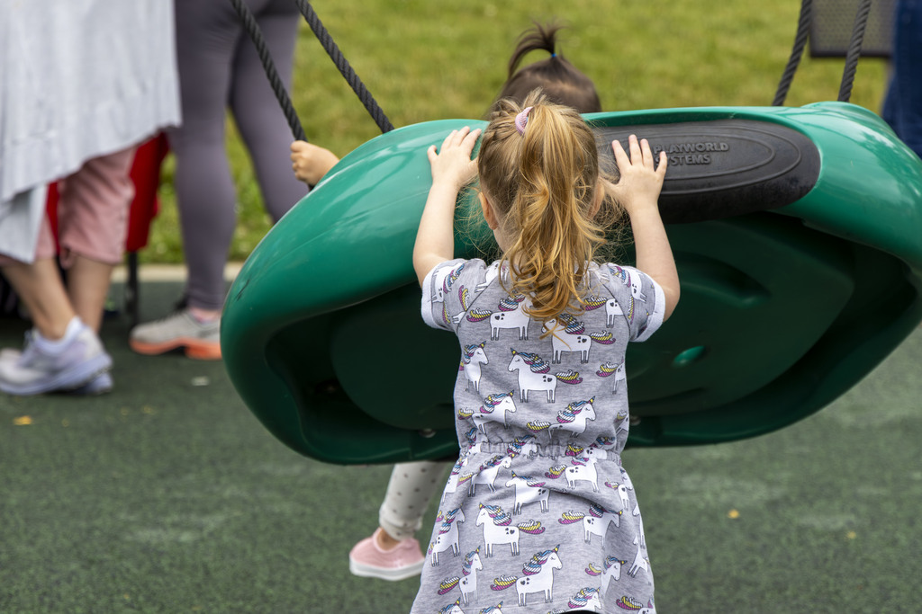 A young girl is pushing another young girl on a big green platform swing at a playground setting.