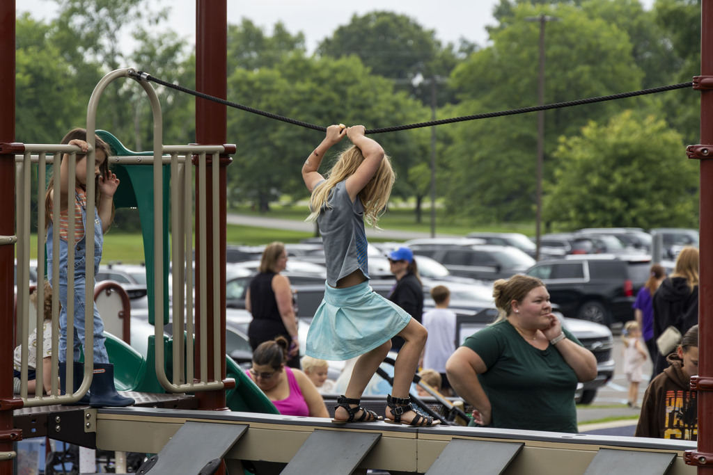 A young girl is holding onto a tightrope at a playground and walking across a thin platform.