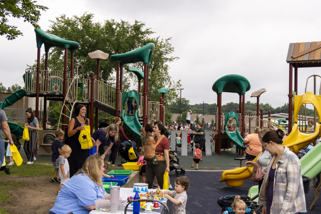 A park full of happy families. Children are playing on the playground and doing crafts. Some parents are talking to one another.