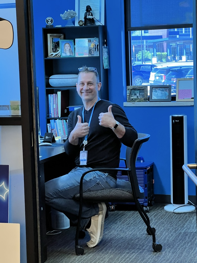Man sitting at his desk giving the camera two thumbs up. 