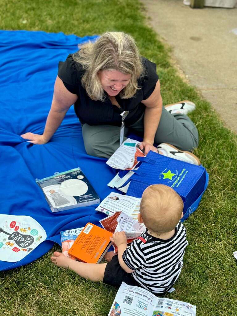 Woman sitting on ground with a toddler looking at books.