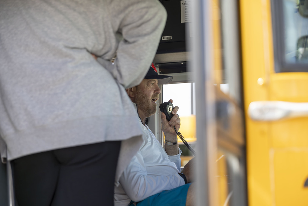 A man wearing a baseball cap speaks into a school bus radio microphone.