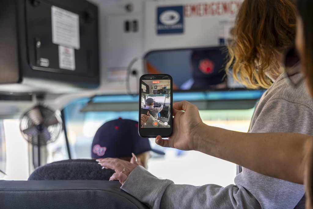 A person uses a smartphone to record a video of a driver operating a school bus.