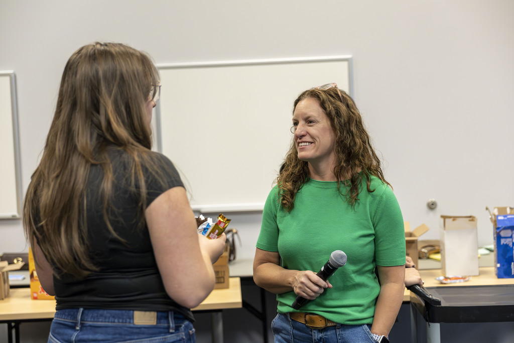 A woman in a green shirt holding a microphone talks with a female student.