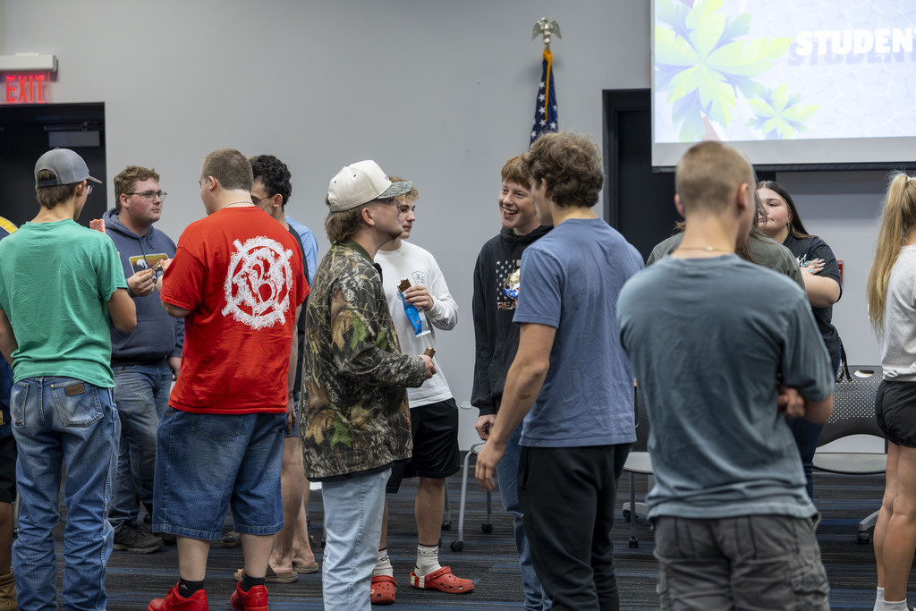 A group of male teenagers talking and eating ice cream bars in a large meeting room.