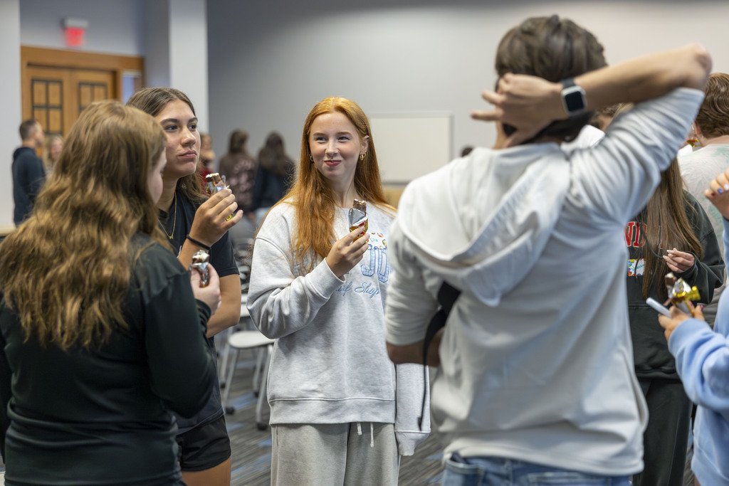 A group of teenagers standing together and socializing while eating ice cream sandwiches. 