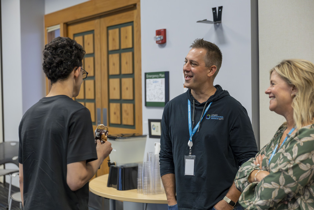 A teenage boy talks to two adults wearing educational agency lanyards.