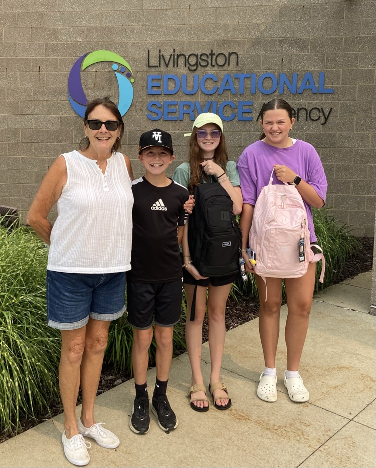 Grandma standing in front of LESA with her grandchildren holding backpacks.