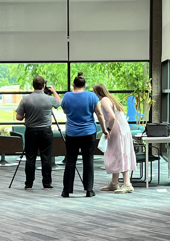 Three adults, one man and two women are setting up a camera on a tripod. 