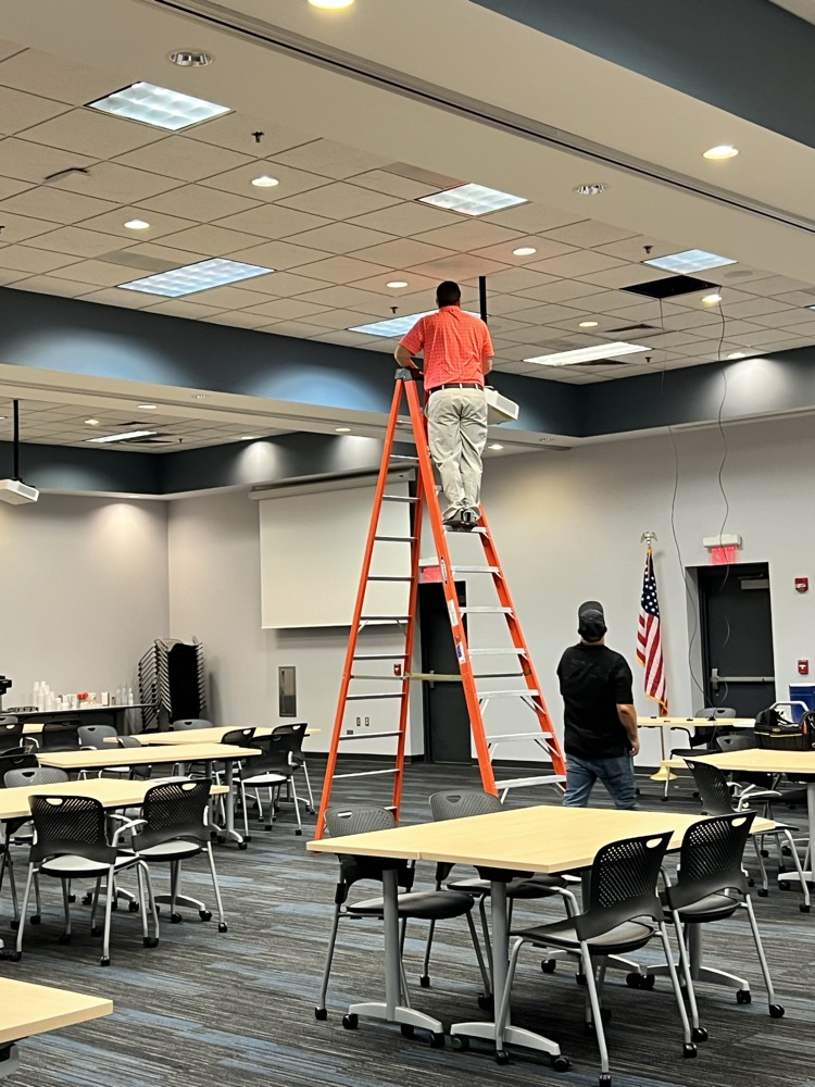 Man standing on tall ladder while another man helps from below. 