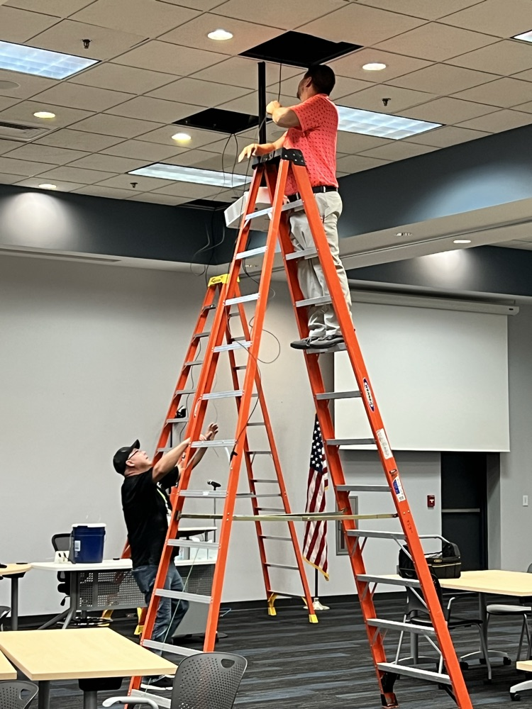 Man standing on tall ladder while another man helps from below. 