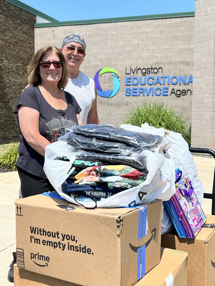 Man and woman stand in front of LESA sign with backpack supplies.
