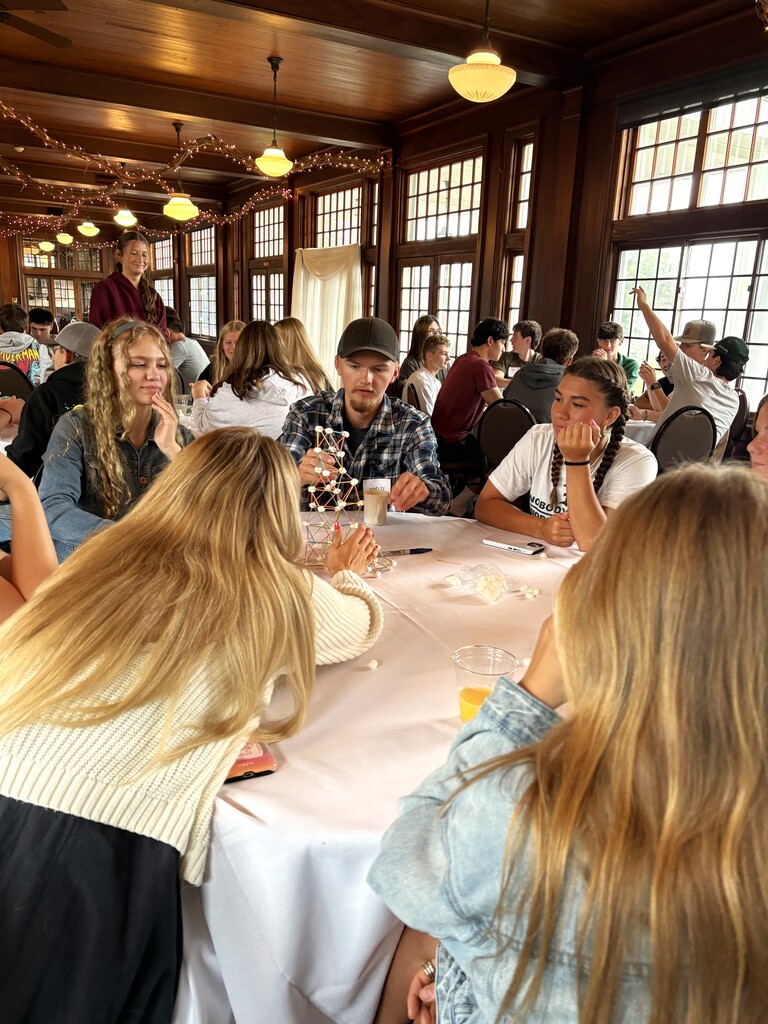 A group of students sitting around a table working together to build a structure out of toothpicks and marshmallows.