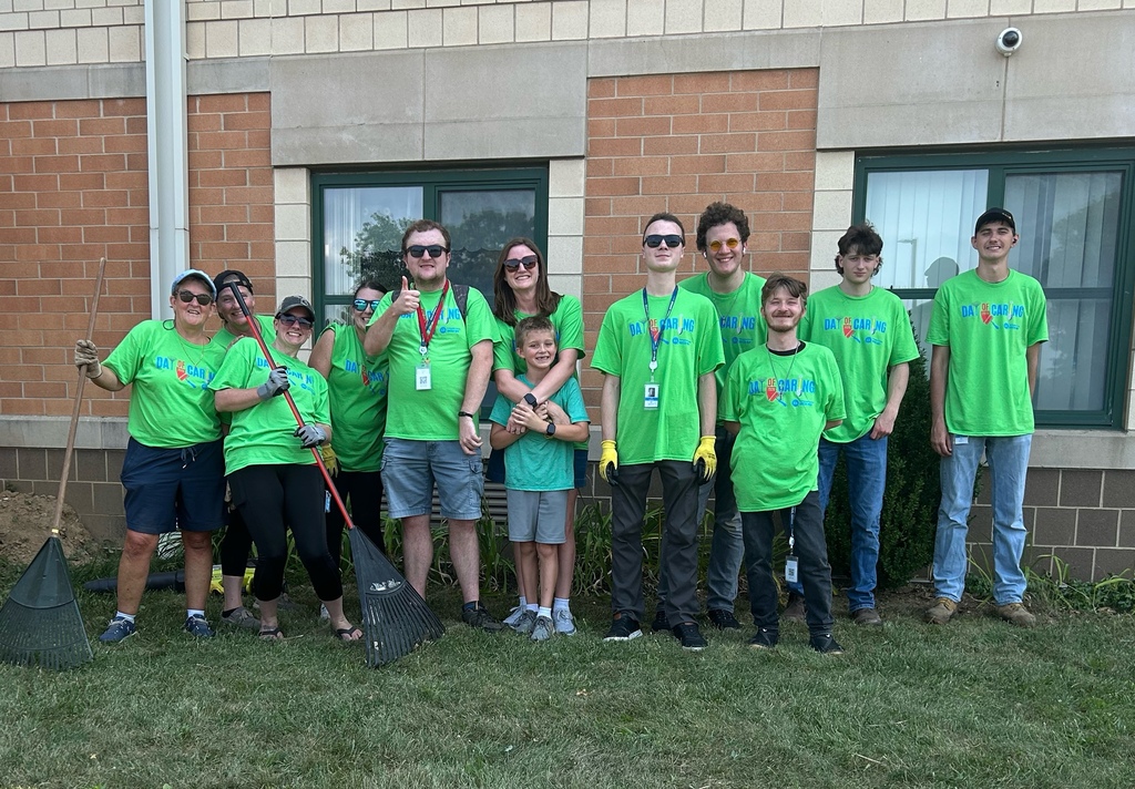 Volunteers holding rakes pose for a group photo outside against a brick wall.